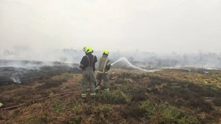 Two people from the firebrigade extinguishing fire on the heath.