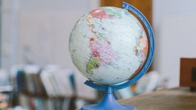 A globe on top of a wooden desk in classroom.