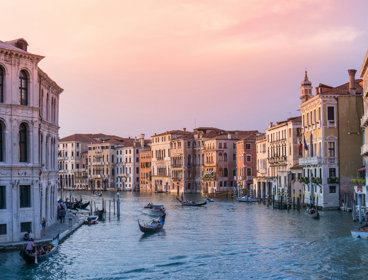 A boat sails down a canal in Venice as the sun sets.