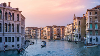 A boat sails down a canal in Venice as the sun sets.