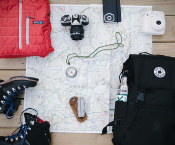 Walking boots, a backpack, compass, folded jacket, digital camera, poloroid camera and note book are all placed on a map