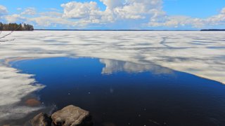 A wide, half frozen lake on a sunny day with only a few clouds in the sky.