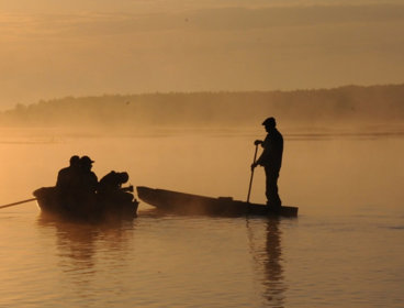 People in two boats on a river at sunset.
