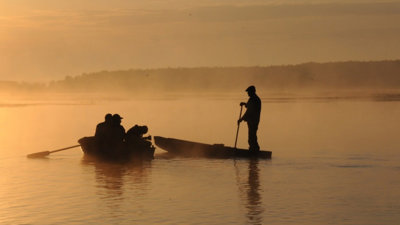 People in two boats on a river at sunset.