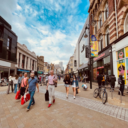 A high street shopping area, with people walking along carrying bags of shopping