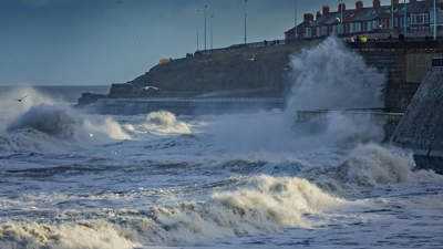 Waves crashing on shore near coastal residences.