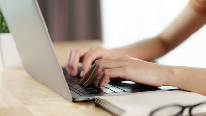 Close up of a person's hands typing on a laptop keyboard.