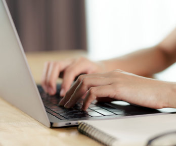 Close up of a person's hands typing on a laptop keyboard.