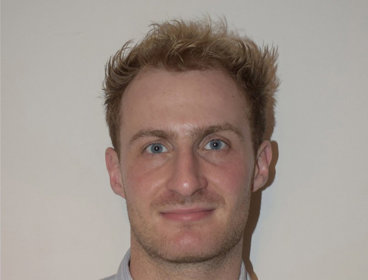 Person wearing a light blue striped button-up shirt against a plain background.