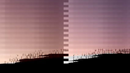 A sillouette of wind farm turbines on a slope with a purple sky