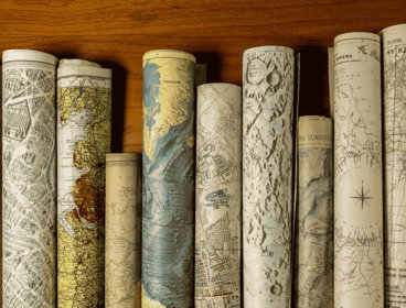 Rolled vintage maps standing upright in a row on a wooden surface.