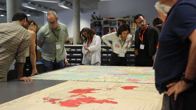 Delegates look at maps spread out on a table in a library.