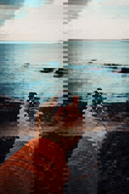 A hand holding a compass with a rocky shore background and ocean
