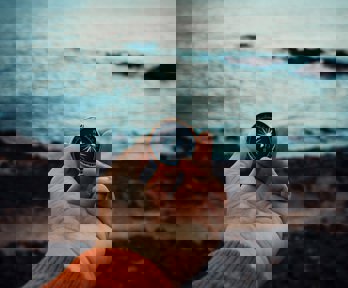 A hand holding a compass with a rocky shore background and ocean