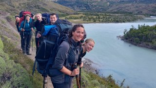 Group of young people wearing trekking gear in an area with mountains and a river.