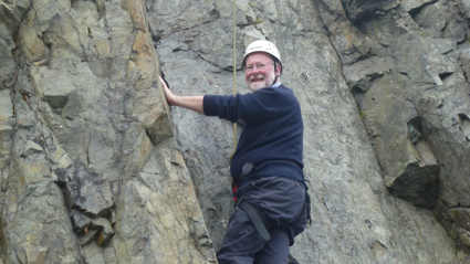 Murray Gray climbing rock wall while looking at the camera with a smile.
