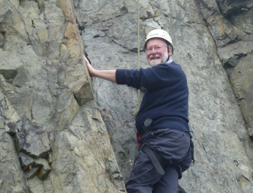 Murray Gray climbing rock wall while looking at the camera with a smile.