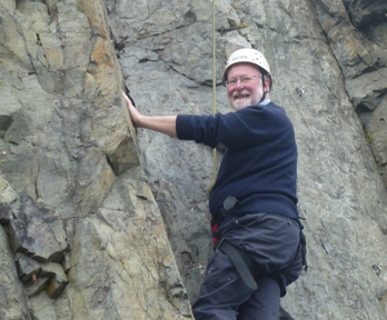 Murray Gray climbing rock wall while looking at the camera with a smile.