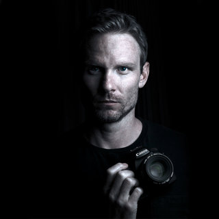 Aaron Gekoski with Canon camera headshot in black and white.