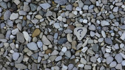 Grey and brown stones on ground, one with question mark.