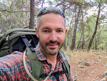 Tom Allen in hiking gear on an unpaved road in a forest.