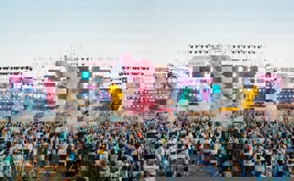 A view over a festival crowd with coloured smoke and bright TV screens