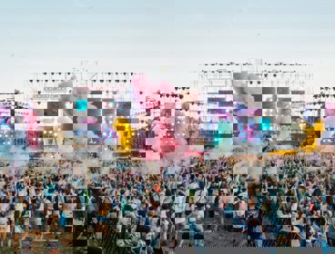 A view over a festival crowd with coloured smoke and bright TV screens