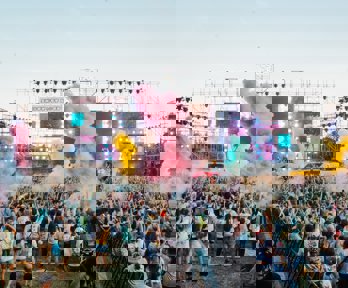 A view over a festival crowd with coloured smoke and bright TV screens