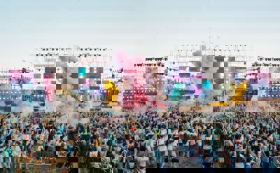 A view over a festival crowd with coloured smoke and bright TV screens