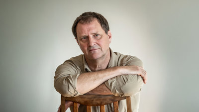 Headshot photo of Simon Townley. He's seated and leaning on a chari with his arms crossed.
