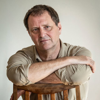 Headshot photo of Simon Townley. He's seated and leaning on a chari with his arms crossed.