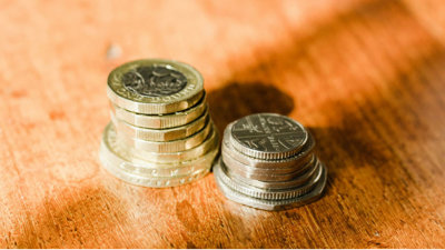 Two piles of British coins stacked up on wooden table.