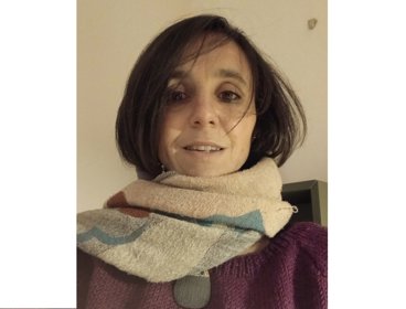 Person wearing a multicolored scarf wrapped around their neck and a purple jumper indoors.