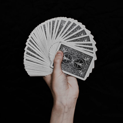 A hand holding a fan of playing cards. The background is black and you cannot see the colourful side of the cards, only the back