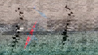 A red kayak in crystal clear blue water seen from above.