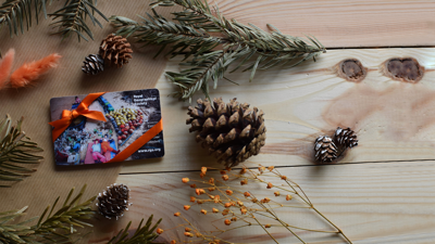 A membership card wrapped up in orange ribbon on a wooden table with festive foliage surrounding it, including acorns and holly.