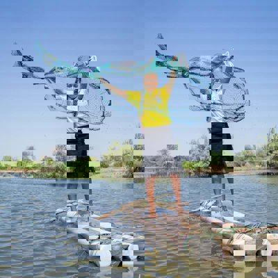 A girl stand on a raft made of three logs, throwing a fishing net into the water