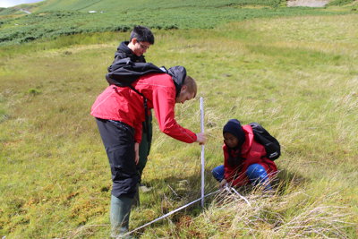 Three people in a field using fieldwork equipment