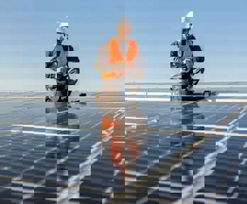 A worker crouching and smiling by some solar panels