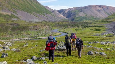 Four backpackers walking alongside a river in a green, mountainous area.