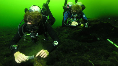 Two SCUBA divers taking samples and making notes underwater.