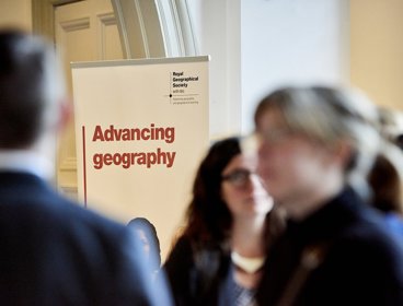Banner with the text 'Advancing geography' and the Society's logo, with blurred figures in the foreground 