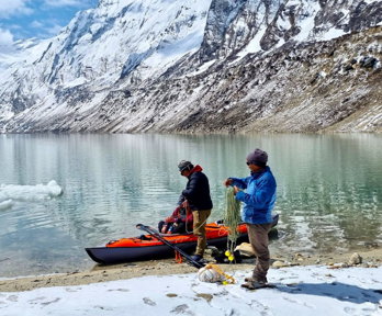 Two researchers on a lakeshore loading submersible temperature sensor arrays into a kayak, with snowclad Nepalese mountains in the background.