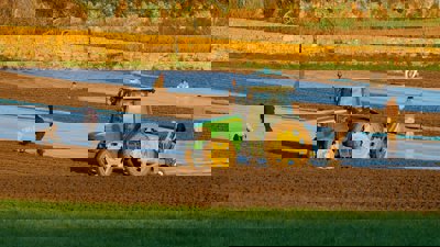 People working in a plowed field with tractor.