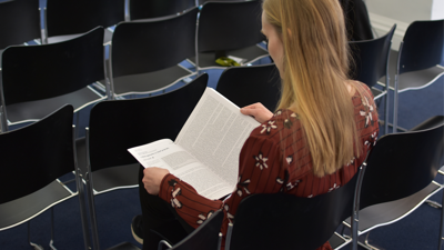 Person reading academic journal on chair surrounded by empty chair.