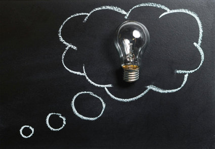 A chalk board with a drawn speech bubble and a real lightbulb