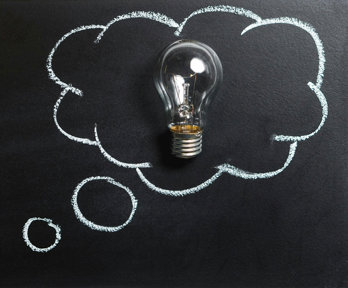 A chalk board with a drawn speech bubble and a real lightbulb