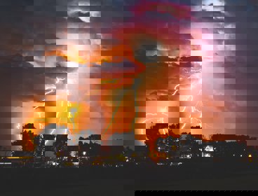 Lightning flashes in an orangey sky over an urban area