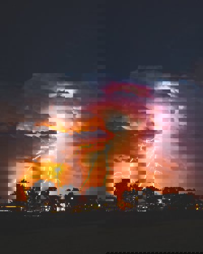 Lightning flashes in an orangey sky over an urban area