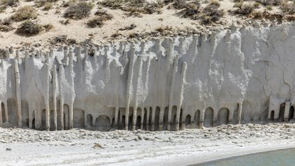 Eroded white limestone cliffs with vertical grooves and sparse vegetation on top beside a calm shoreline.